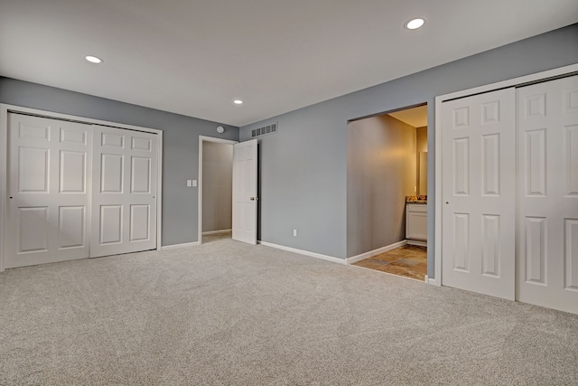 unfurnished bedroom featuring light colored carpet and two closets