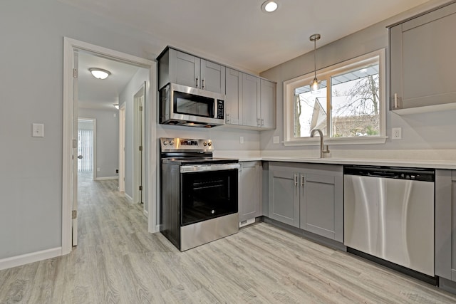 kitchen featuring gray cabinetry, stainless steel appliances, sink, pendant lighting, and light hardwood / wood-style flooring