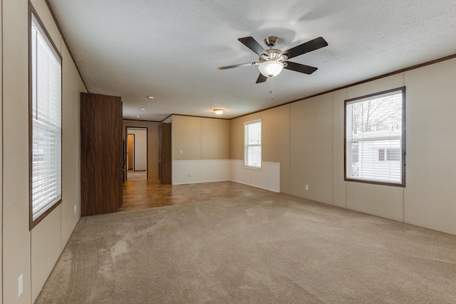 carpeted empty room featuring ornamental molding, a ceiling fan, and a textured ceiling