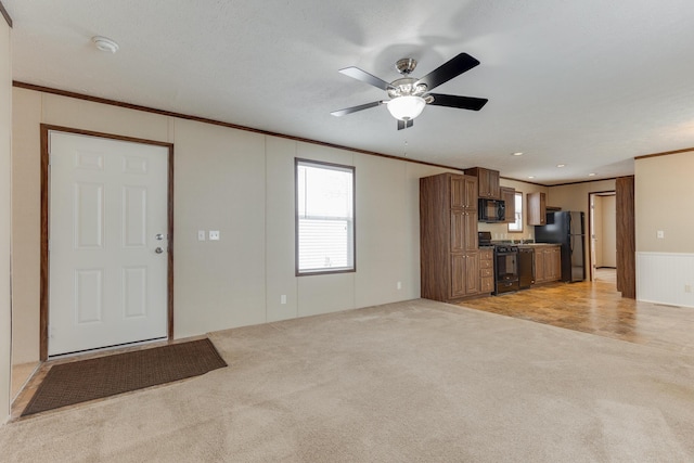unfurnished living room with ornamental molding, ceiling fan, wainscoting, and light carpet