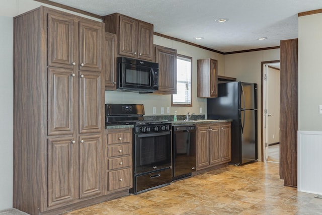 kitchen featuring a sink, dark countertops, crown molding, black appliances, and a wainscoted wall