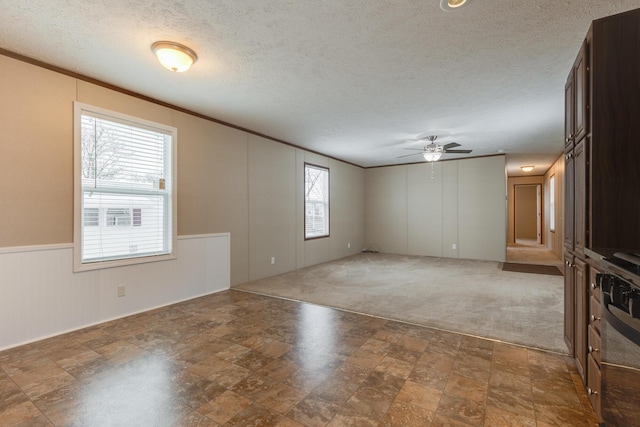carpeted empty room with wainscoting, a textured ceiling, ornamental molding, and ceiling fan