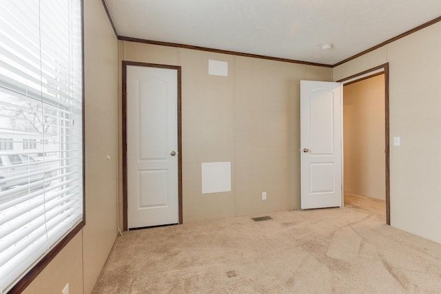 unfurnished bedroom with carpet flooring, visible vents, multiple windows, and ornamental molding