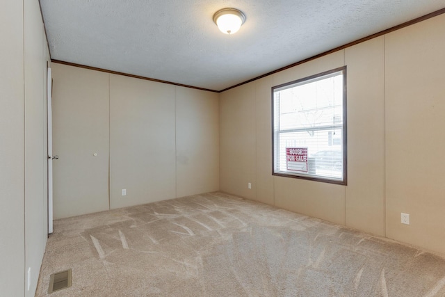 carpeted spare room featuring visible vents, a textured ceiling, and ornamental molding