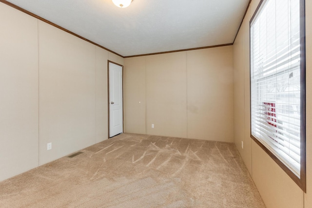 empty room featuring visible vents, light colored carpet, and ornamental molding