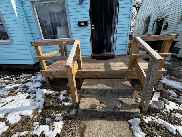 snow covered property entrance featuring a wooden deck