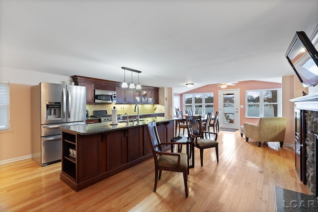 kitchen with decorative backsplash, appliances with stainless steel finishes, dark brown cabinetry, pendant lighting, and light hardwood / wood-style floors