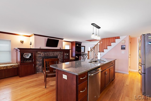 kitchen featuring sink, hanging light fixtures, stainless steel appliances, an island with sink, and a fireplace