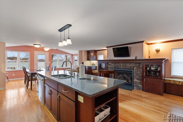 kitchen featuring dark stone counters, a kitchen island with sink, sink, a fireplace, and hanging light fixtures