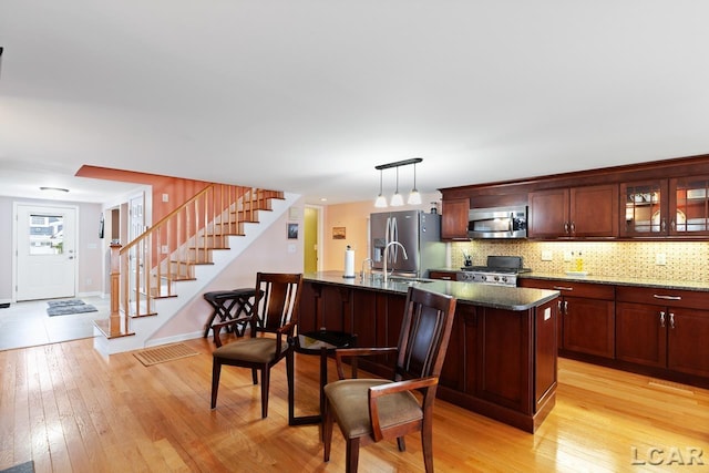 kitchen with tasteful backsplash, light hardwood / wood-style flooring, decorative light fixtures, a kitchen island with sink, and appliances with stainless steel finishes