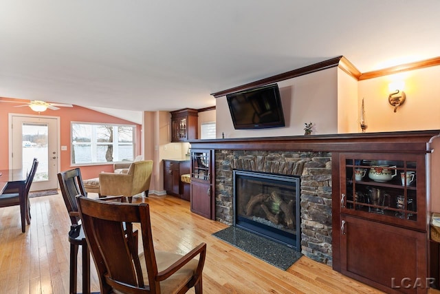 dining room featuring a stone fireplace, ceiling fan, light hardwood / wood-style flooring, and ornamental molding