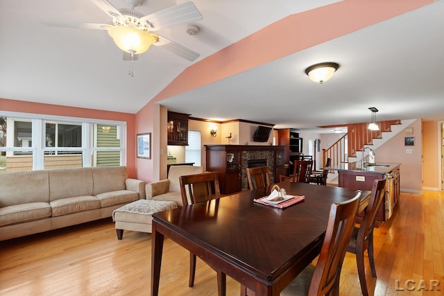 dining area featuring ceiling fan, sink, a stone fireplace, light hardwood / wood-style floors, and lofted ceiling