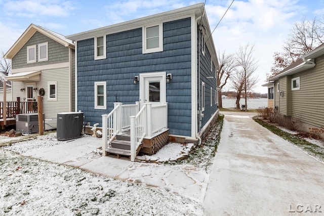 snow covered rear of property featuring central AC unit