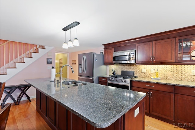 kitchen featuring sink, stainless steel appliances, an island with sink, dark stone counters, and pendant lighting