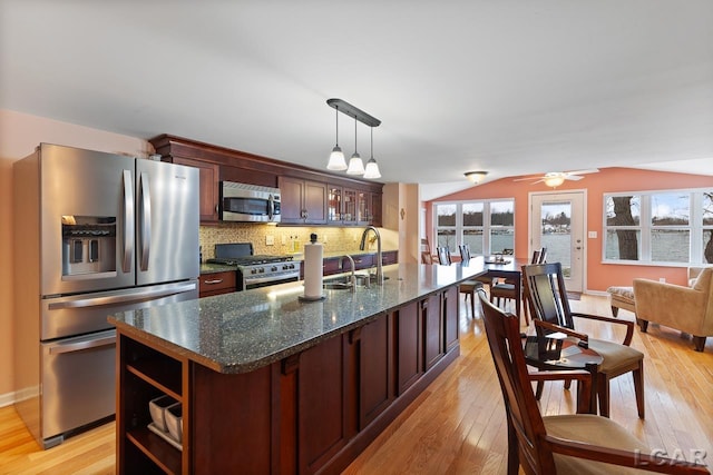 kitchen with backsplash, a kitchen island with sink, hanging light fixtures, sink, and appliances with stainless steel finishes