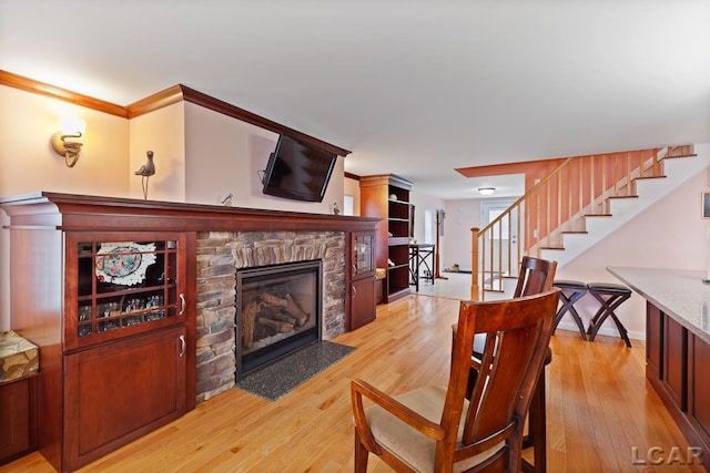 living room featuring a stone fireplace, light wood-type flooring, and crown molding