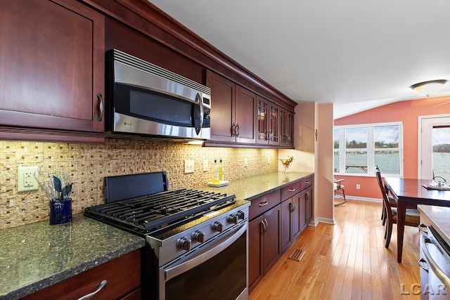 kitchen with stainless steel appliances, backsplash, dark stone counters, lofted ceiling, and light wood-type flooring