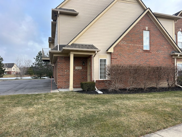 view of front facade featuring roof with shingles, a front yard, and brick siding