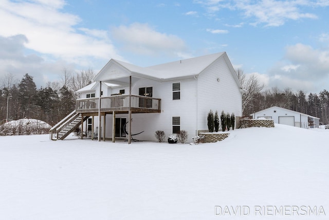 snow covered back of property with a garage, an outdoor structure, and a deck