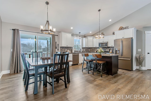 dining room with vaulted ceiling, a healthy amount of sunlight, an inviting chandelier, and light wood-type flooring