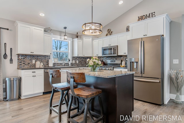 kitchen with vaulted ceiling, appliances with stainless steel finishes, a kitchen island, pendant lighting, and white cabinets