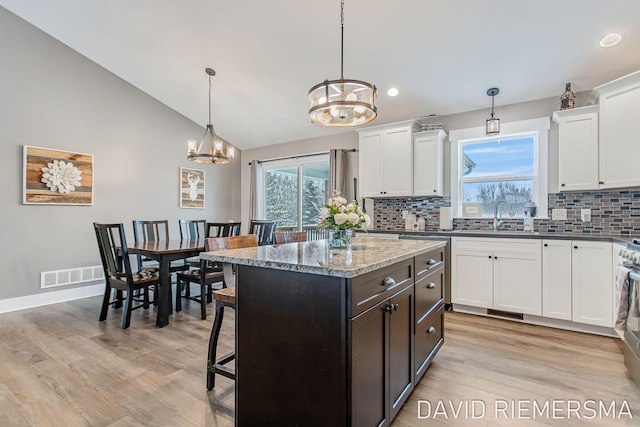 kitchen with pendant lighting, a kitchen island, decorative backsplash, vaulted ceiling, and a chandelier