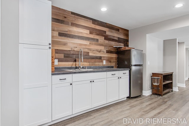 kitchen with stainless steel refrigerator, wooden walls, sink, and white cabinets