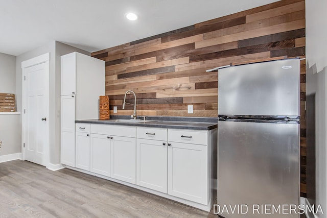 kitchen with sink, stainless steel fridge, white cabinetry, wooden walls, and light wood-type flooring