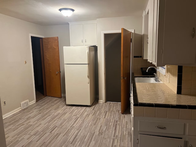 kitchen with white cabinetry, sink, decorative backsplash, white refrigerator, and tile counters