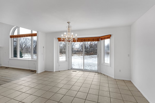 empty room with light tile patterned floors, a notable chandelier, and a healthy amount of sunlight