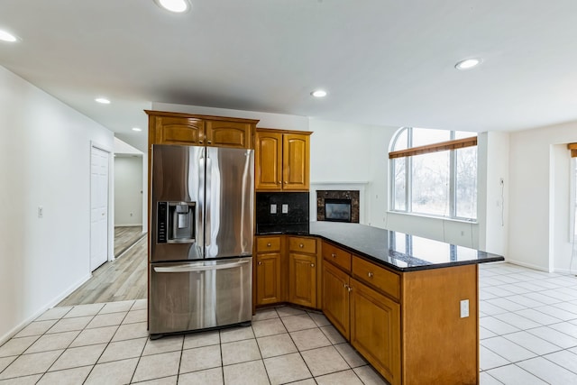 kitchen featuring dark stone counters, kitchen peninsula, decorative backsplash, light tile patterned flooring, and stainless steel fridge with ice dispenser