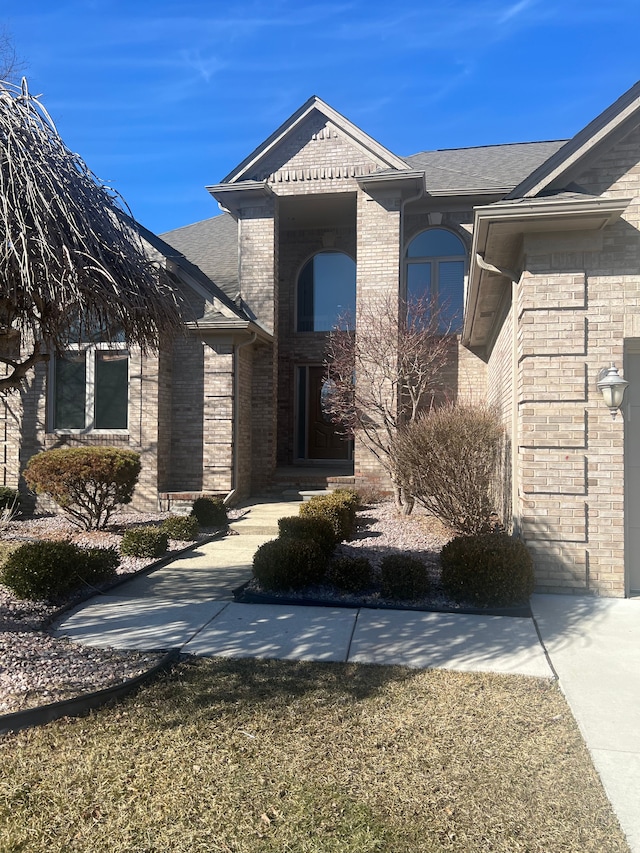 property entrance featuring brick siding and roof with shingles