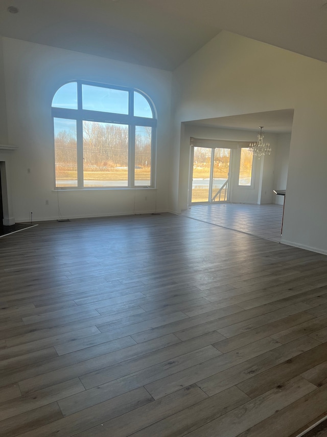 unfurnished living room featuring high vaulted ceiling, a fireplace with raised hearth, dark wood finished floors, baseboards, and a chandelier