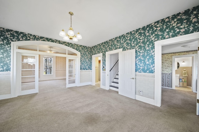 empty room featuring ceiling fan with notable chandelier, french doors, and carpet floors