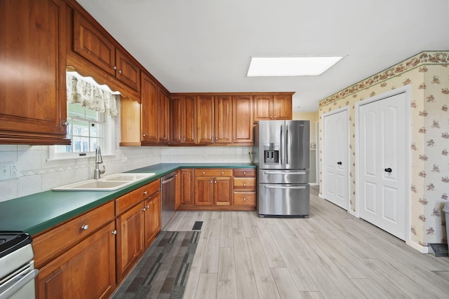 kitchen featuring a skylight, sink, light hardwood / wood-style flooring, backsplash, and appliances with stainless steel finishes