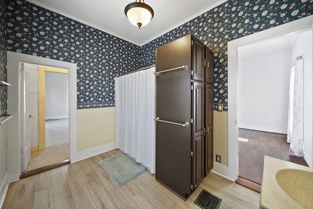 kitchen featuring dark brown cabinetry, light hardwood / wood-style floors, and ornamental molding