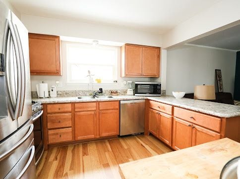 kitchen featuring kitchen peninsula, appliances with stainless steel finishes, light wood-type flooring, light stone countertops, and sink