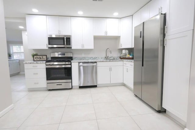 kitchen featuring light stone countertops, appliances with stainless steel finishes, sink, white cabinets, and light tile patterned flooring