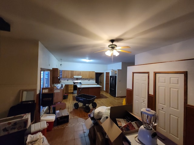 kitchen featuring stainless steel range with electric cooktop, exhaust hood, refrigerator, ceiling fan, and a kitchen island