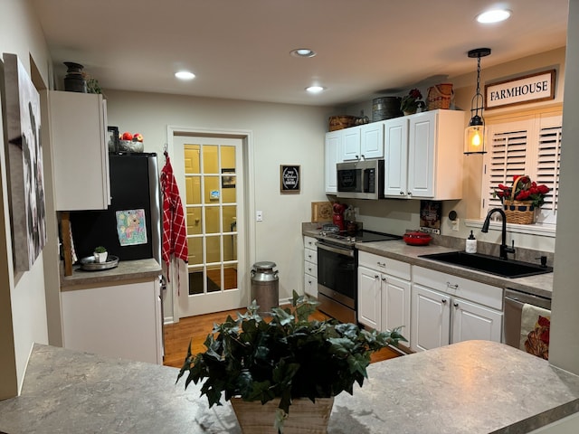 kitchen featuring hanging light fixtures, sink, stainless steel appliances, and white cabinetry