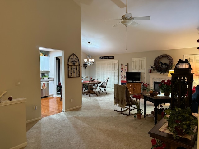 living room featuring a fireplace, light colored carpet, ceiling fan with notable chandelier, and high vaulted ceiling