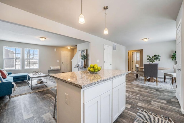 kitchen featuring white cabinetry, a center island, light stone counters, dark hardwood / wood-style flooring, and decorative light fixtures