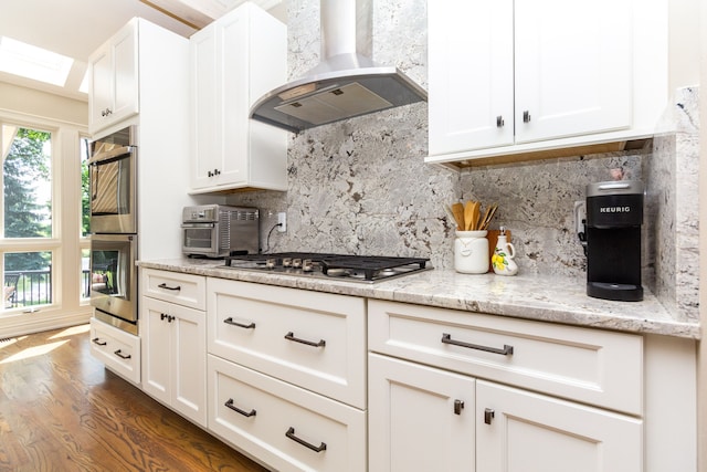 kitchen with exhaust hood, dark wood-type flooring, stainless steel appliances, light stone counters, and white cabinetry