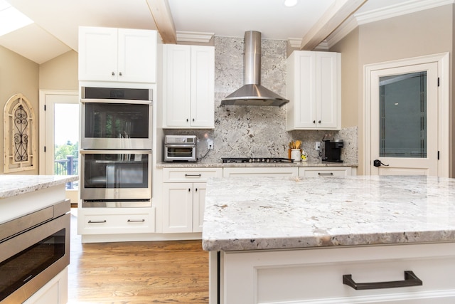 kitchen featuring appliances with stainless steel finishes, white cabinets, light stone countertops, and wall chimney range hood