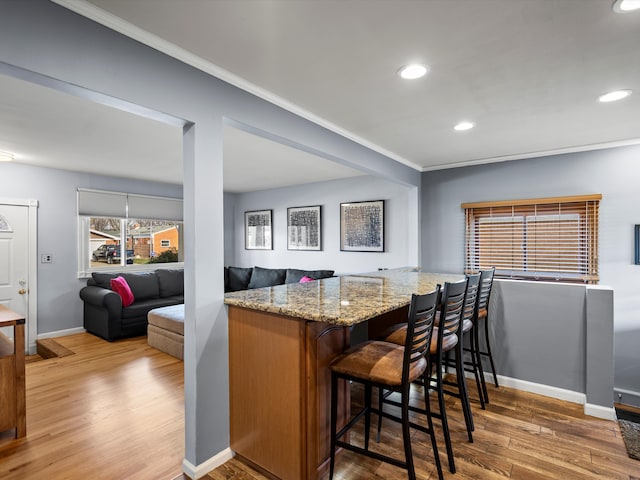 kitchen with light stone countertops, kitchen peninsula, crown molding, hardwood / wood-style floors, and a breakfast bar area