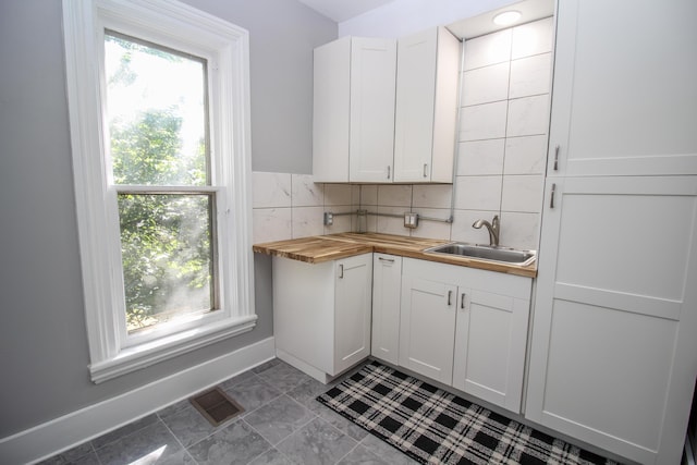 kitchen with butcher block countertops, decorative backsplash, white cabinetry, and sink