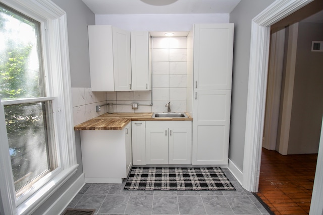 kitchen with butcher block countertops, white cabinetry, tasteful backsplash, and sink