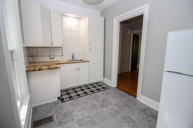 kitchen with white cabinetry, sink, white fridge, and wood counters