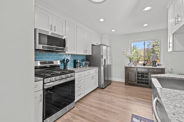 kitchen featuring light stone countertops, stainless steel appliances, backsplash, white cabinets, and light wood-type flooring