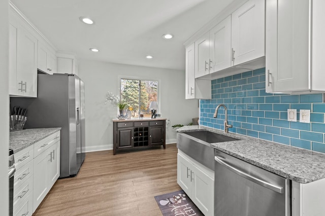 kitchen with appliances with stainless steel finishes, light stone counters, sink, light hardwood / wood-style flooring, and white cabinets